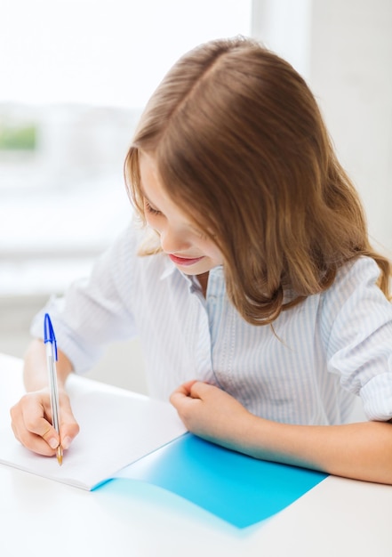 concept d'éducation et d'école - petite étudiante écrivant dans un cahier à l'école