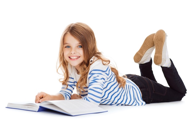 concept d'éducation et d'école - petite étudiante souriante avec un livre allongé sur le sol