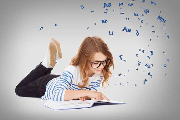 concept d'éducation et d'école - petite étudiante souriante avec un livre et des lunettes allongé sur le sol