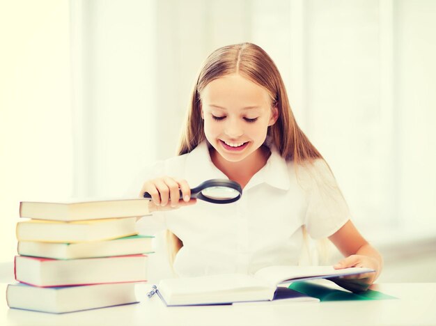 concept d'éducation et d'école - petite fille étudiante lisant un livre avec une loupe à l'école