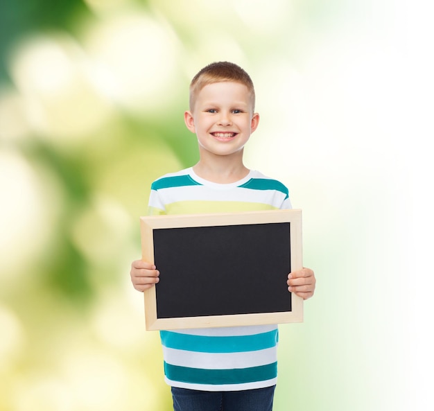 Concept d'éducation, d'école, de publicité, d'écologie et de personnes - petit garçon souriant tenant un tableau noir vierge sur fond vert