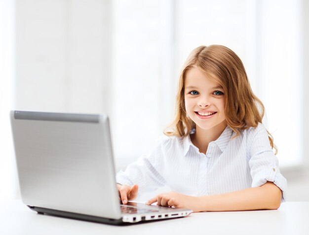 concept d'éducation, d'école, de technologie et d'internet - petite étudiante avec un ordinateur portable à l'école