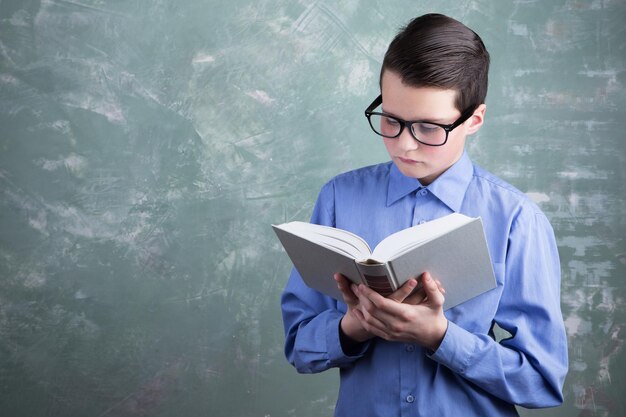 Concept d'éducation écolier dans des verres lisant un livre sur fond de grange verte