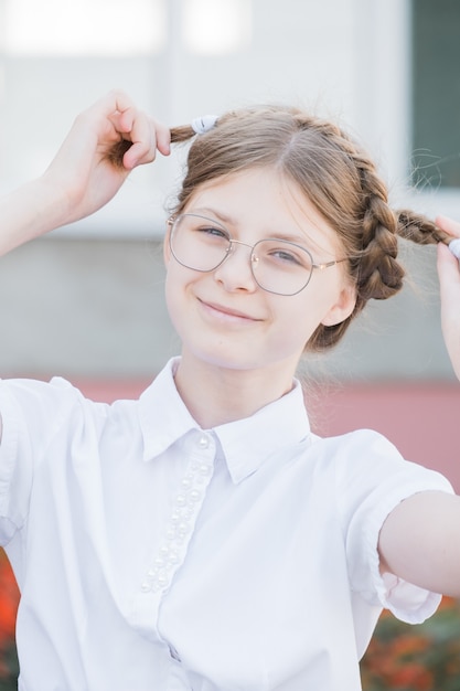 Photo le concept d'éducation. élève de l'école primaire à lunettes en uniforme s'amuser avec des nattes et sourire. fille drôle dans des verres prête pour l'école.