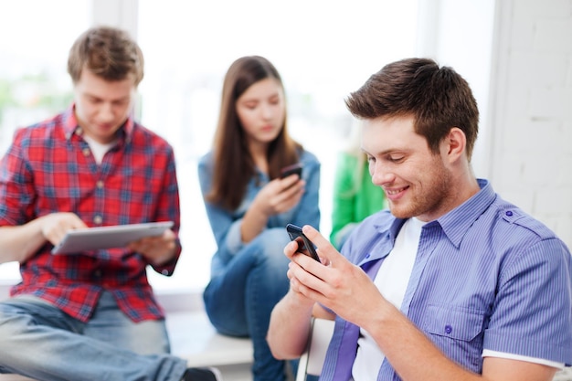 concept d'éducation - étudiant regardant dans le téléphone et écrivant à l'école