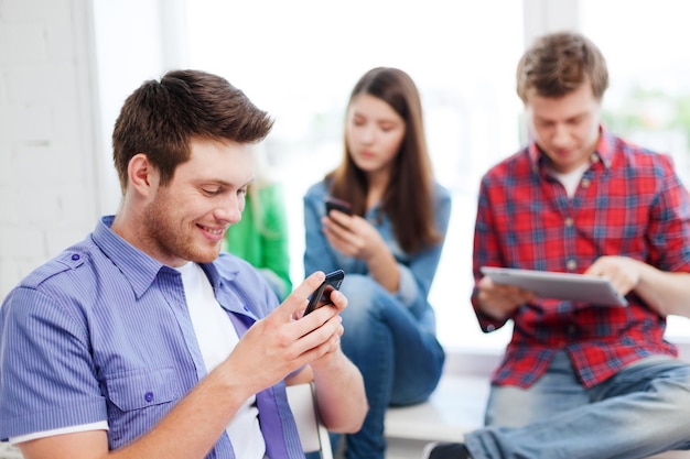 concept d'éducation - étudiant regardant dans le téléphone et écrivant à l'école