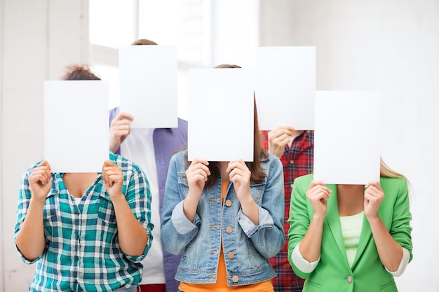concept d'éducation - groupe d'étudiants couvrant les visages avec des papiers vierges