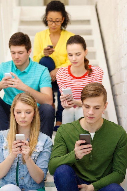 Photo concept d'éducation, de loisirs et de technologie - étudiants occupés avec des smartphones assis sur l'escalier