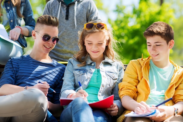 concept d'éducation, de lycée et de personnes - groupe d'étudiants adolescents heureux avec des cahiers apprenant dans la cour du campus