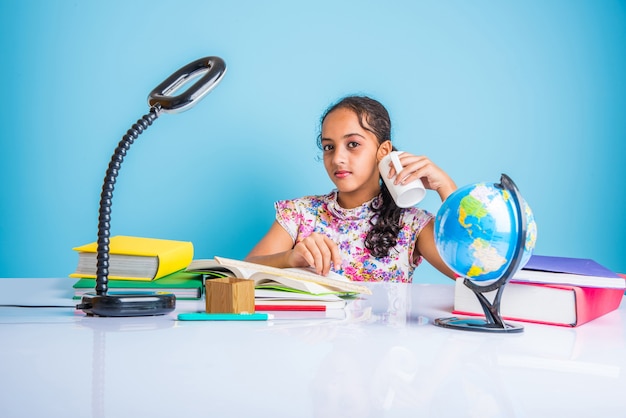 Concept d'éducation à la maison - Jolie petite fille indienne ou asiatique qui étudie à la maison avec une pile de livres, un globe éducatif, etc. Mise au point sélective