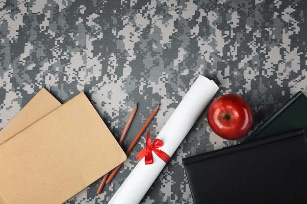 Photo concept d'éducation militaire livres crayons rouleaux papier et pomme sur fond de camouflage