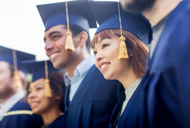 concept d'éducation, d'obtention du diplôme et de personnes - groupe d'étudiants internationaux heureux dans des planches de mortier et des robes de célibataire en plein air