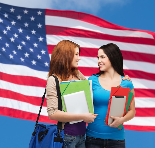 concept d'éducation et de personnes - deux étudiants souriants avec sac et dossiers se regardant sur fond de drapeau américain