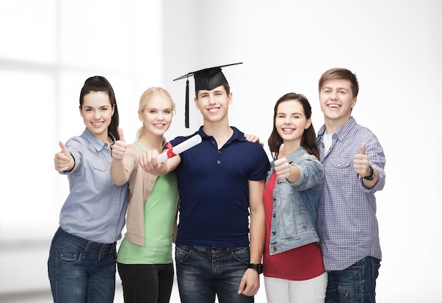 concept d'éducation et de personnes - groupe d'étudiants souriants debout avec diplôme et coin-cap montrant les pouces vers le haut