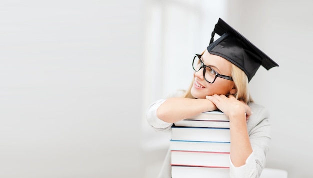 concept d'éducation - photo d'un étudiant heureux en chapeau de graduation avec une pile de livres