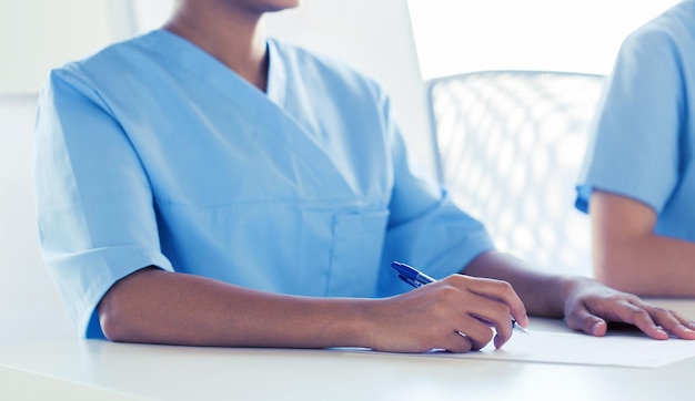 Photo concept d'éducation, de profession, de personnes et de médecine - gros plan de médecins écrivant sur du papier lors d'une conférence à l'hôpital