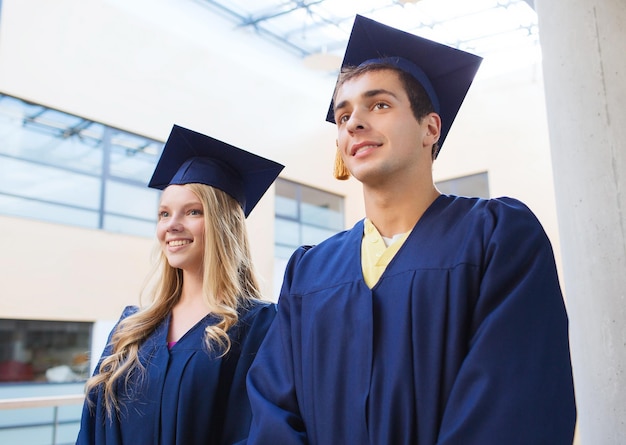 concept d'éducation, de remise des diplômes et de personnes - groupe d'étudiants souriants dans des mortiers et des robes à l'extérieur