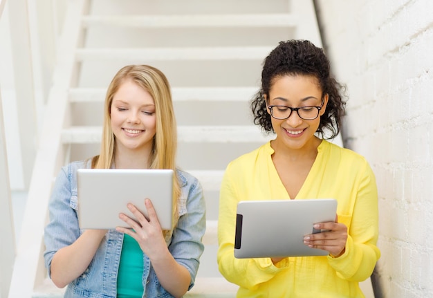 concept d'éducation et de technologie - étudiantes souriantes avec ordinateur tablette pc assis sur l'escalier