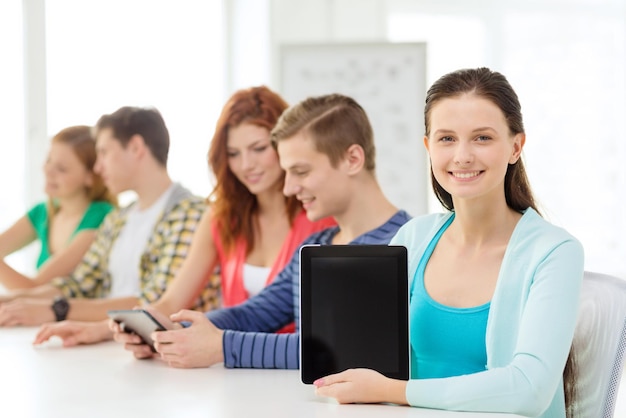 concept d'éducation, de technologie et d'internet - adolescente souriante devant des étudiants montrant un écran vierge d'un ordinateur tablette à l'école