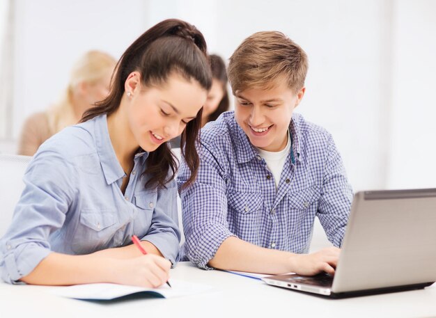 concept d'éducation, de technologie et d'internet - deux étudiants souriants avec ordinateur portable et cahiers à l'école