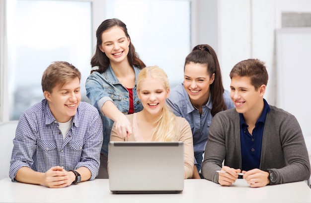 concept d'éducation, de technologie et d'internet - étudiants souriants regardant et pointant vers un ordinateur portable à l'école