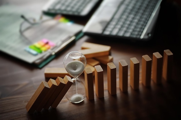 Concept d'effet Domino avec des tuiles en bois bloquées par un sablier avec fond