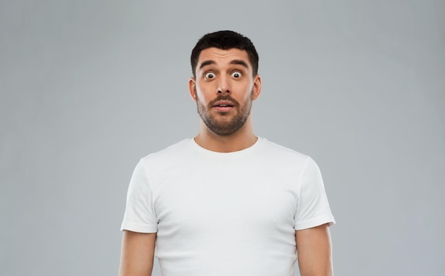 Photo concept d'émotion, de publicité et de personnes - homme effrayé en t-shirt blanc sur fond gris