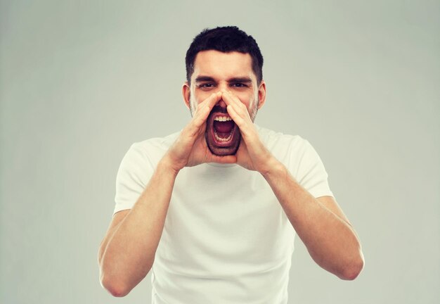 concept d'émotions, de communication et de personnes - homme criant en colère en t-shirt sur fond gris