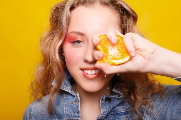 Concept d'émotions, de santé, de personnes, de nourriture et de beauté - Beauty Model Girl prend des oranges juteuses. Belle adolescente joyeuse avec des taches de rousseur, coiffure drôle. maquillage jaune. Maquillage professionnel. Tranche d'orange