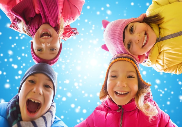 concept d'enfance, d'amitié, d'hiver, de noël et de personnes - de petits enfants heureux font face à l'extérieur sur fond de ciel bleu et de neige