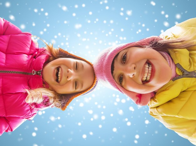 concept d'enfance, d'amitié, de noël, d'hiver et de personnes - des petites filles heureuses font face à l'extérieur sur fond de ciel bleu et de neige