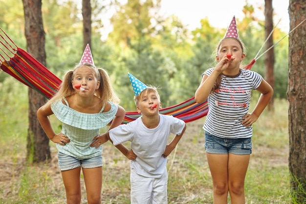 Concept d'enfance et de célébration d'anniversaire enfants heureux soufflant des cornes de fête et s'amusant en été à l'extérieur