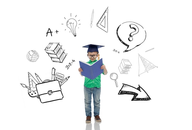 concept d'enfance, d'école, d'éducation, d'apprentissage et de personnes - garçon heureux en chapeau de célibataire ou mortier et lunettes lisant un livre avec des griffonnages