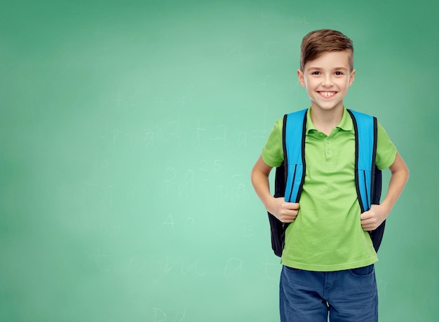 Photo concept d'enfance, d'école, d'éducation et de personnes - heureux garçon étudiant souriant avec sac d'école sur fond de tableau de craie d'école verte