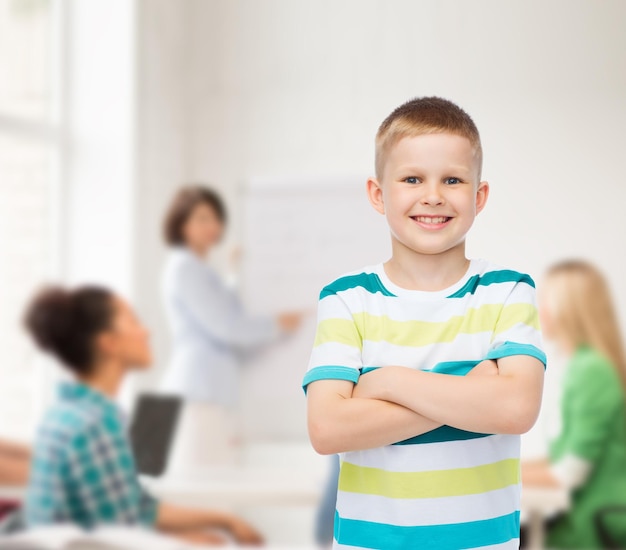concept d'enfance, d'école, d'éducation et de personnes - petit garçon souriant dans des vêtements décontractés avec les bras croisés sur un groupe d'élèves en classe