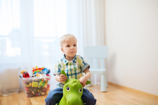 concept d'enfance, de jouets et de personnes - petit garçon heureux jouant avec un cheval jouet à cheval à la maison