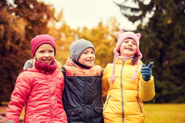 concept d'enfance, de loisirs, d'amitié et de personnes - groupe d'enfants heureux embrassant et pointant du doigt quelque chose dans le parc d'automne