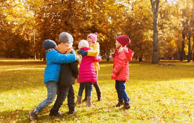 concept d'enfance, de loisirs, d'amitié et de personnes - groupe d'enfants heureux s'embrassant dans le parc d'automne