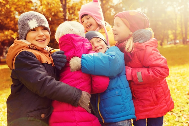 concept d'enfance, de loisirs, d'amitié et de personnes - groupe d'enfants heureux s'embrassant dans le parc d'automne