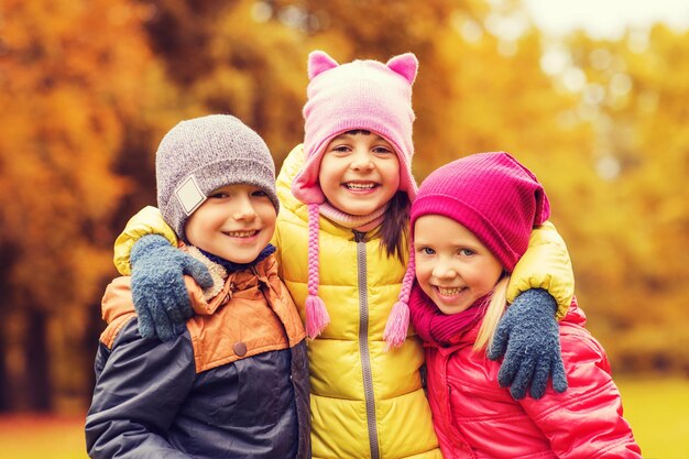 concept d'enfance, de loisirs, d'amitié et de personnes - groupe d'enfants heureux s'embrassant dans le parc d'automne