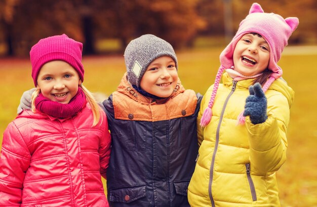 Photo concept d'enfance, de loisirs, d'amitié et de personnes - groupe d'enfants heureux s'embrassant et pointant le doigt sur vous dans le parc d'automne