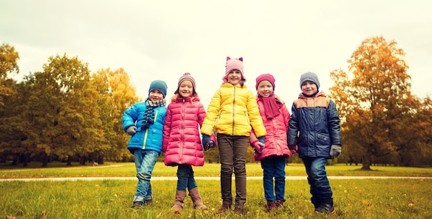 concept d'enfance, de loisirs, d'amitié et de personnes - groupe d'enfants heureux se tenant la main dans le parc d'automne