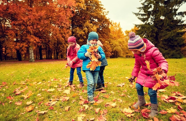 concept d'enfance, de loisirs, d'automne, d'amitié et de personnes - groupe d'enfants ramassant des feuilles dans le parc