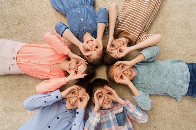 concept d'enfance, de mode, d'amitié et de personnes - enfants heureux allongés en cercle sur le sol, faisant des grimaces et s'amusant