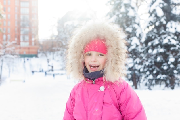 Concept de l'enfance, de la mode, de la saison et des personnes - Petite fille 4K jouant dans la neige en hiver, voir un enfant heureux faisant une boule de neige, un bonhomme de neige, des enfants en vacances de Noël. visage de fille heureuse en vêtements d'hiver