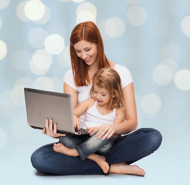 concept d'enfance, de parentalité et de technologie - mère heureuse avec une adorable petite fille et un ordinateur portable sur fond de lumières de vacances