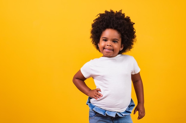 Concept d'enfance et de personnes - heureuse petite fille afro-américaine sur fond jaune. Petite fille noire aux cheveux noirs souriants.