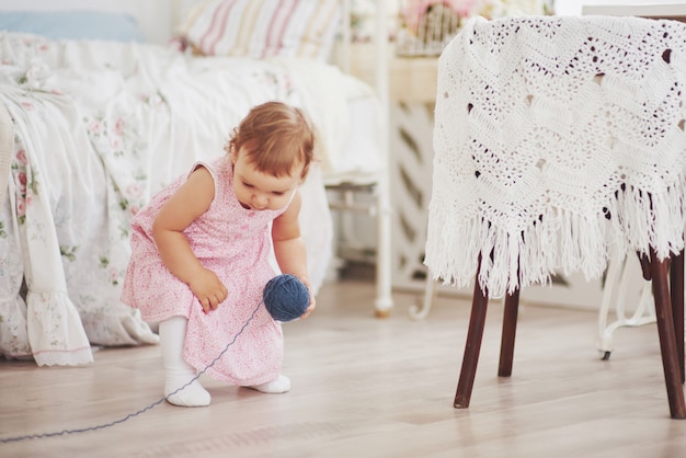 Concept d'enfance. Petite fille en robe mignonne joue avec du fil de couleur. Chambre d'enfant vintage blanche