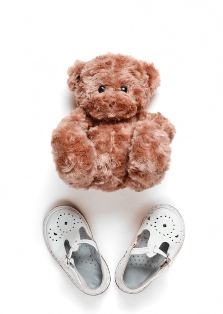 Le concept de l'enfance. Sandales pour enfants en cuir blanc, ours en peluche sur blanc