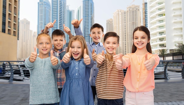 concept d'enfance, de voyage, de tourisme, de geste et de personnes - garçon et filles souriants heureux montrant les pouces vers le haut sur fond de rue de la ville de dubaï